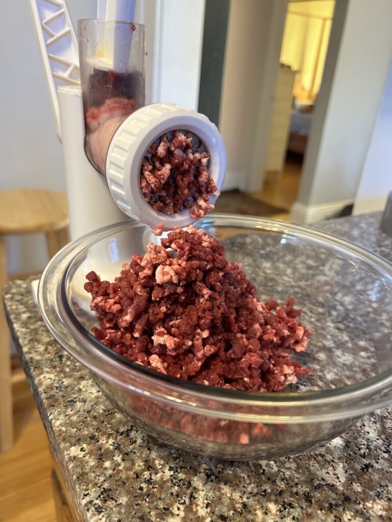 Meat grinder grinding up beef heart into a clear bowl