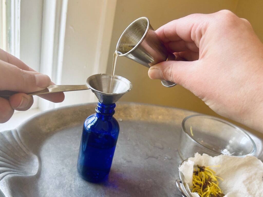 Blue Glass bottle on metal tray. Pouring brandy into bottle of lower essence
