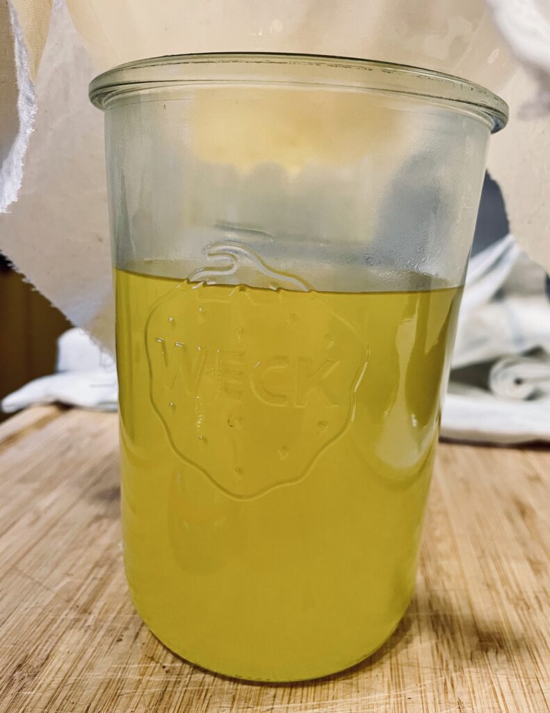 Golden beef tallow being strained through linen into glass jar
