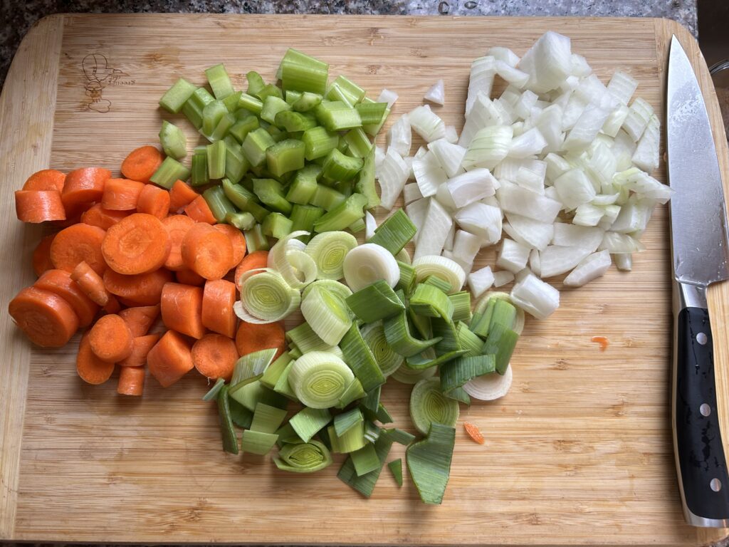 Mirepoix with leek added on cutting board with chef knife.