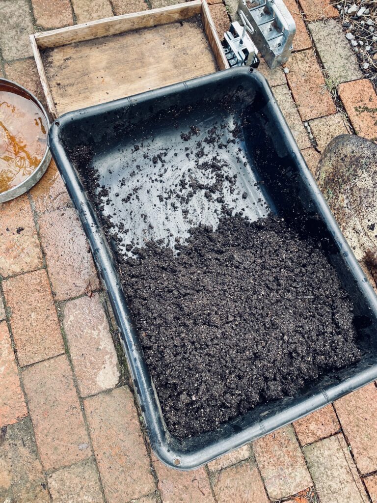 Soil mix in black plastic tray. Soil block maker and wooden seed tray