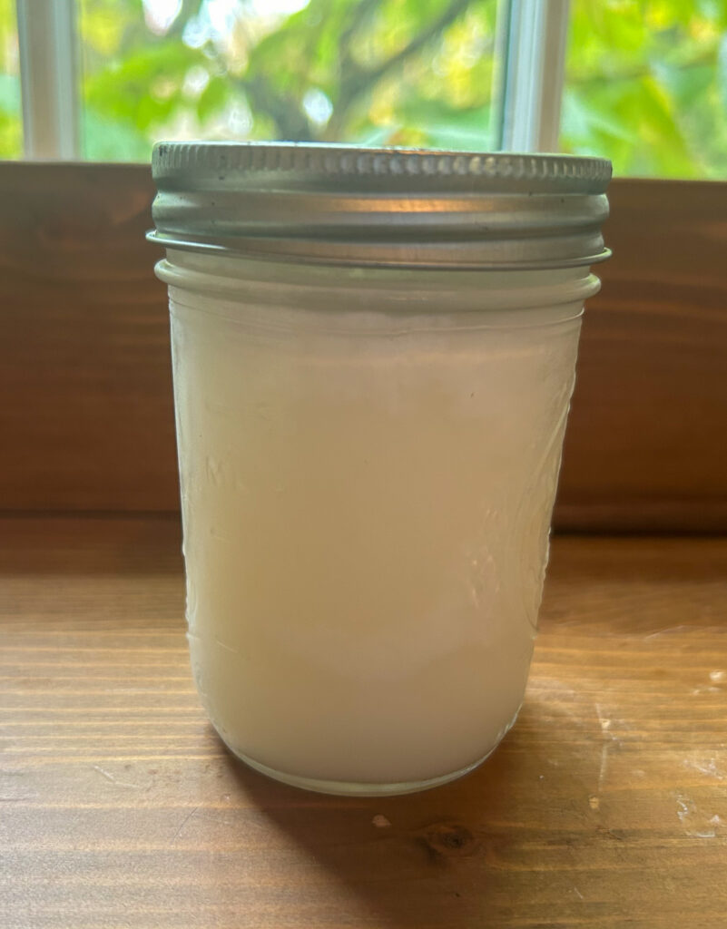 Jar of lard from first rendering. Sitting on wooden shelf with window in the background. 