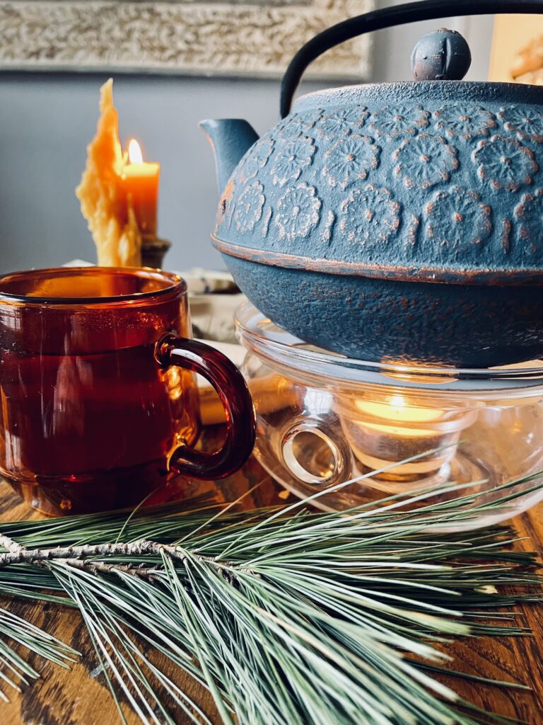 amber glass cup, blue teapot, yellow candle, pine needles